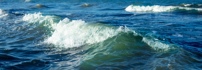 A small wave at sea. Blue sea water and white crest of the wave.