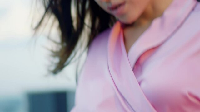 At terrace on the roof top woman in the evening time holding her pink robe while she is outside and it s windy closeup to the camera