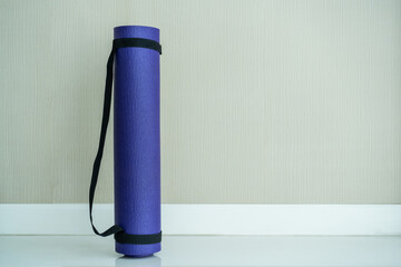 Rolled purple yoga exercise mat on the floor in living room.