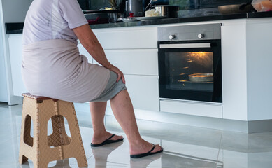 Granny is waiting front of the electric oven to finish cooking in