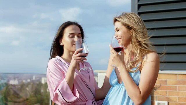 In front of the camera portrait of a beautiful excited women enjoying the time in pajamas they drink some glass of wine and smiling large on the roof top of loft apartment
