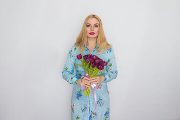 Blonde woman in floral dress holding purple tulips in her hands