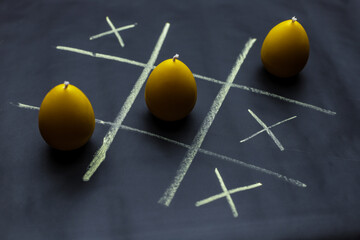 Playing tic tac toe or noughts and crosses with candles in the form of eggs.