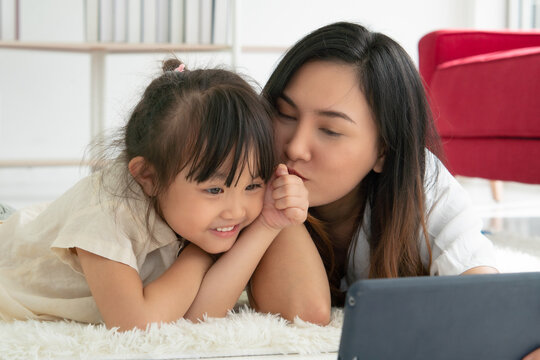 asian kid kissing her mom while the mother using tablet to taking photo of them in living room. family together concept