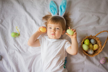 Cute funny baby with bunny ears and colorful Easter eggs at home on a white background