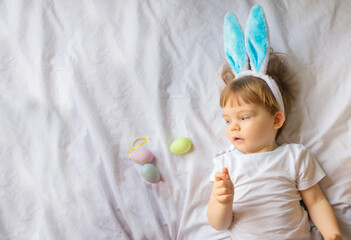 Obraz na płótnie Canvas Cute funny baby with bunny ears and colorful Easter eggs at home on a white background