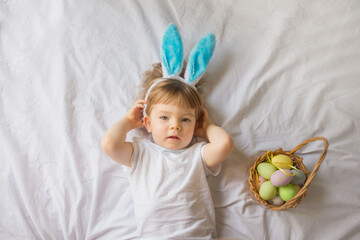 Cute funny baby with bunny ears and colorful Easter eggs at home on a white background