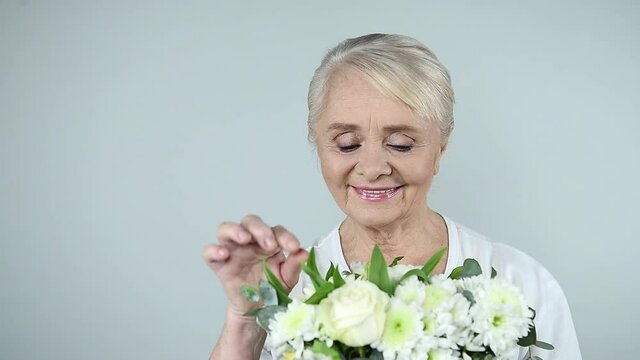 Pensive older woman smelling bouquet of beautiful flowers