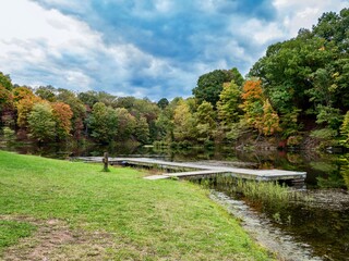 Tomlinson Run State Park in the fall in West Virginia with the fall colors and trees reflecting in the lake, the blue cloud filled sky in the background and a tranquil serene nature landscape scene.