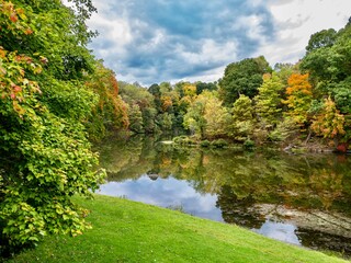 Tomlinson Run State Park in the fall in West Virginia with the fall colors and trees reflecting in the lake, the blue cloud filled sky in the background and a tranquil serene nature landscape scene.