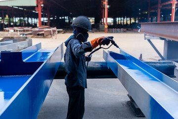 The painter is working to painting color top coat on steel structure with spray gun, at industrial factory.