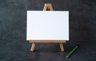 wooden easel with white board with space for text and green pencil on gray background