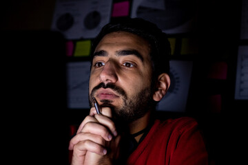 Young man is thinking in front of his laptop at the overtime hours in his dark office