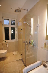 Blick in ein Bad mit einer modernen minimalistischen Dusche. Die Fliesen sind beige und glänzend