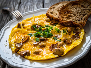 Delicious breakfast - scrambled eggs with fried champignon and chive on wooden table
