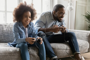 Happy gamer dad and kid playing online computer video game, relaxing on couch in living room....