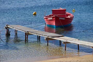 A red fishing boat near tiny quay in crystal clear sea, Greece