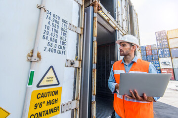 Confident Caucasian man engineer wearing white safety helmet using computer laptop and check for control loading containers box from Cargo freight ship for import and export, transport
