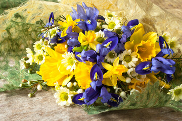 A bouquet of daffodils, irises and chrysanthemums in decorative paper packaging on the table, close-up.