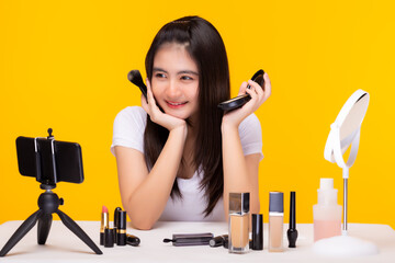Teenage girl blogger present beauty product and broadcasting live video on social network at home by using smart phone Influencer beautician woman talking to audience Holding foundation, makeup brush