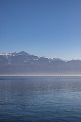 A boat on hazy, misty Lake Geneva and the Alps seen from Lausanne, Switzerland