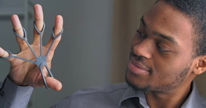 Portrait of afro american business man taking break from work uses gray sports equipment mini trainer for sports unclenches fingers trains hand with expander strains muscles rehabilitates injured arm