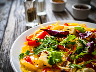 Delicious breakfast - scrambled eggs with onion, bell pepper, feta cheese and mix of young vegetable leaves on wooden table
