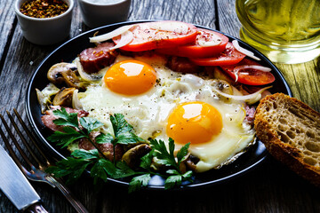 Sunny side up eggs with spinach, toasted bread and sausages on wooden table
