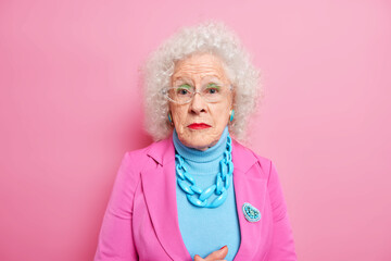 Portrait of serious mature grey haired woman dressed in elegant clothes with jewelry wears makeup...
