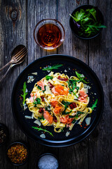 Tagliatelle with salmon nuggets, arugula and sun-dried tomatoes on wooden table
