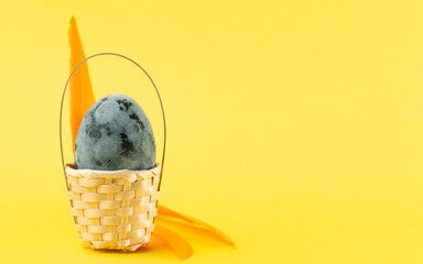 Easter egg in basket decorated with feathers on a yellow background. Easter holiday concept. Copy space, close up