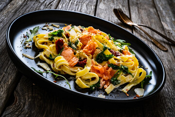 Tagliatelle with salmon nuggets, arugula and sun-dried tomatoes on wooden table
