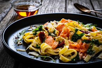 Tagliatelle with salmon nuggets, arugula and sun-dried tomatoes on wooden table
