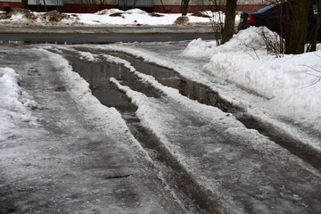 The beginning of spring or winter thaw. Roadway with large puddles and holes. Dirty ice and snow on...