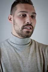 Portrait of a young brown-haired man with a short beard and a gray turtleneck sweater	
