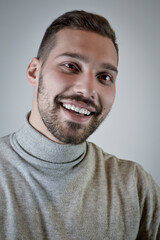 Portrait of a smiling young brown-haired man with a short beard and a gray turtleneck sweater	