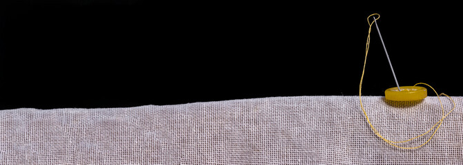 A banner with a gray piece of stiff fabric to which a yellow button is sewn with a sewing needle...