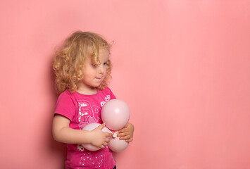 Portrait of  2-year-old girl with balloons on a pink pastel background