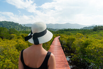 Woman hiking red painted wood trail path along mangrove forest, Thailand