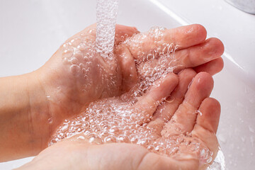 Fototapeta premium Children's hands under the running water from the faucet in the bathroom.