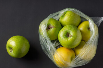 Fototapeta na wymiar Transparent plastic crumpled cellophane bag with group of ripe green and yellow apples on a black background. Ecology concept