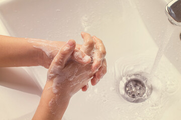 Fototapeta premium washing children's soapy hands under running water in the sink.