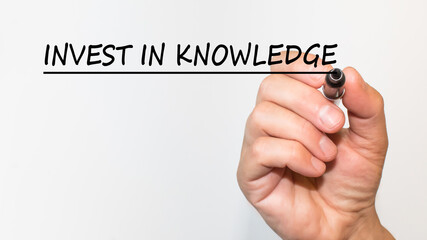 the hand writes text INVEST IN KNOWLEDGE with a marker on a white background. business concept