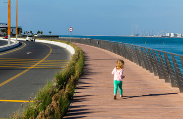 little girl running on a boardwalk next to the road. Outdoors