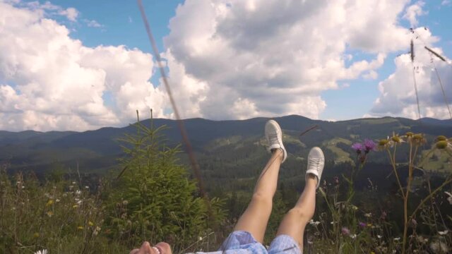 Young woman falling in drass and blooming flowers in summer Carpathian mountains on meadow. Happy and free girl having fun enjoying landscape
