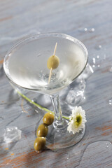 Classic martini mixed in a shaker with gin, dry vermouth, ice and green olives for garnish.