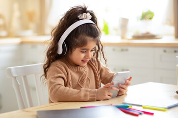Kids And Gadgets. Cute Little Girl In Wireless Headphones Playing With Smartphone