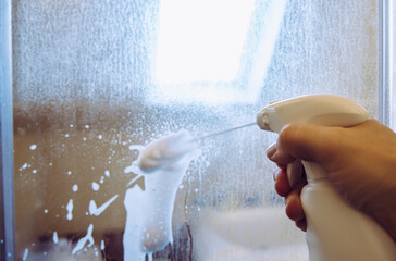 Person hand using limescale remover chemical foam. Descaling shower case glass door. Work in...