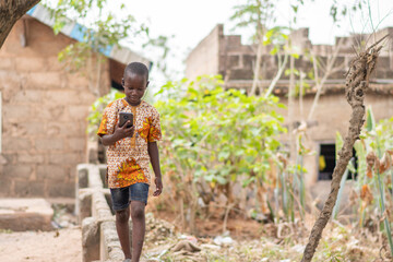 african kid walking on a short fence while using a phone and wearing headphones, listening to music