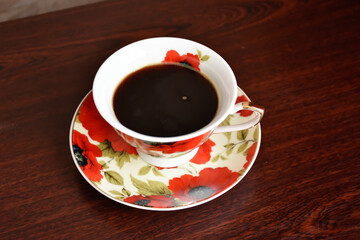 Red poppy cup of coffee with the saucer on the dark wooden table.